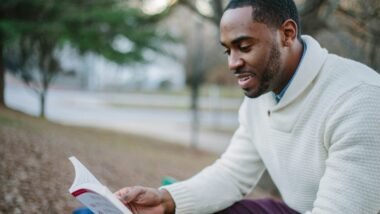 man wearing white sweater while reading book